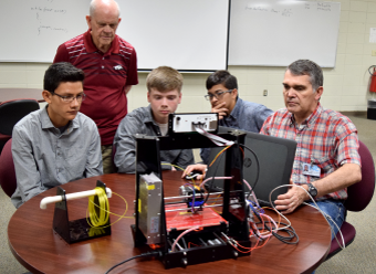 Students and teachers from the Hot Springs Middle School sitting with the black 3D printer on the table.