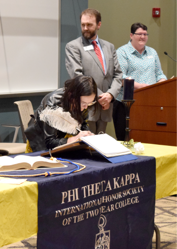 PTK inductee Anna Archer signing the pledge book during the spring induction ceremony at National Park College as Dr. Wade Derden and Dr. Rebekah Robinette welcome the inductees.