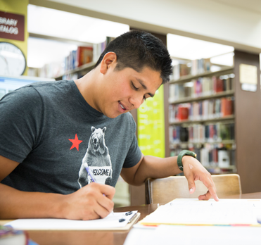 Person sitting in a library looking at a book and taking notes.