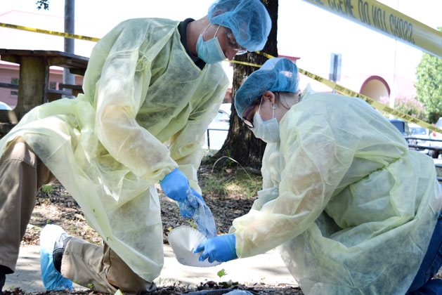 Two people in personal protective equipment at a mock crime scene.