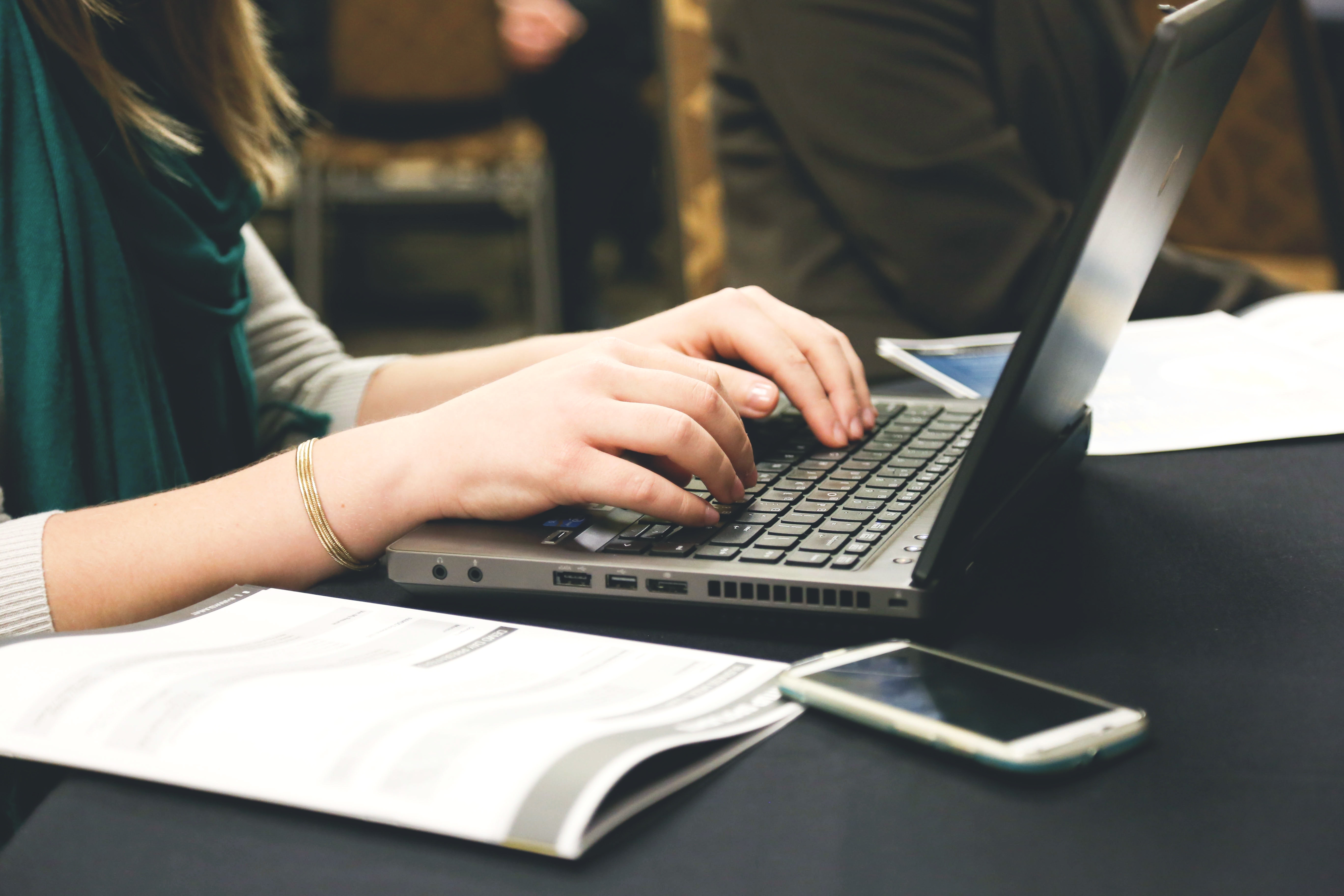 Woman typing on laptop with paper and phone sitting next to her