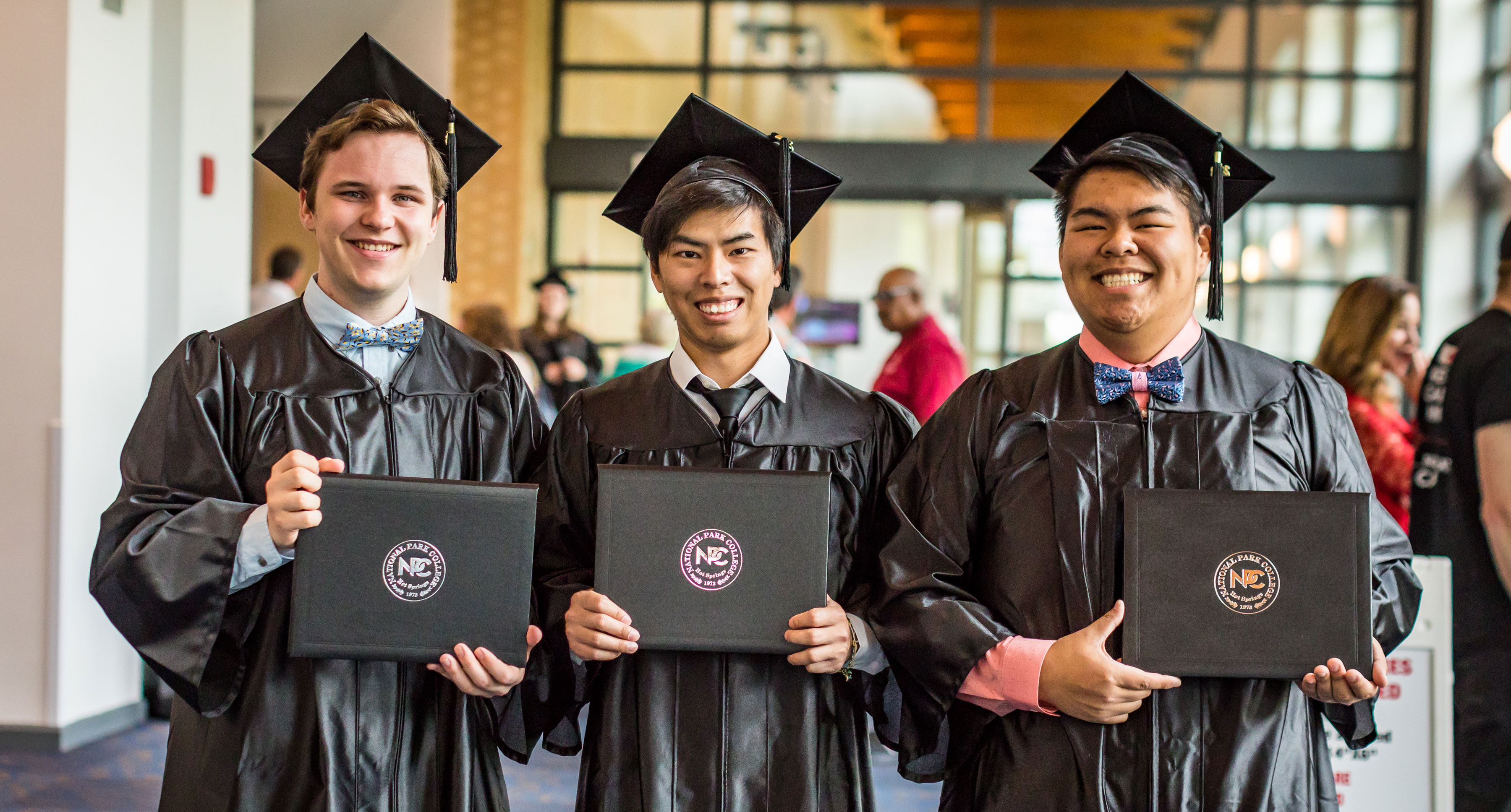 Three male graduates smiling and holding their diplomas