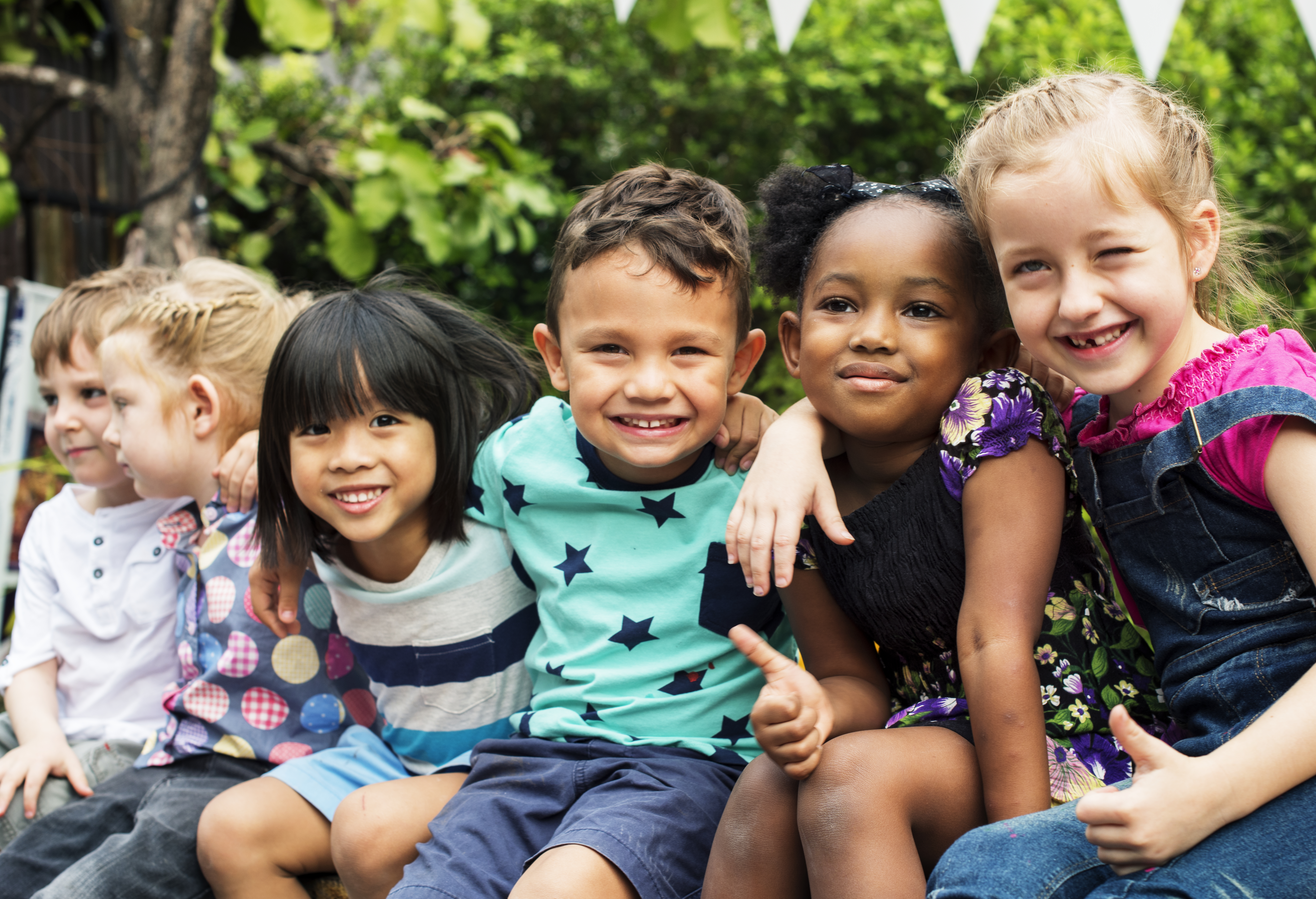 Kids sitting with arms wrapped around each other shoulders and smiling