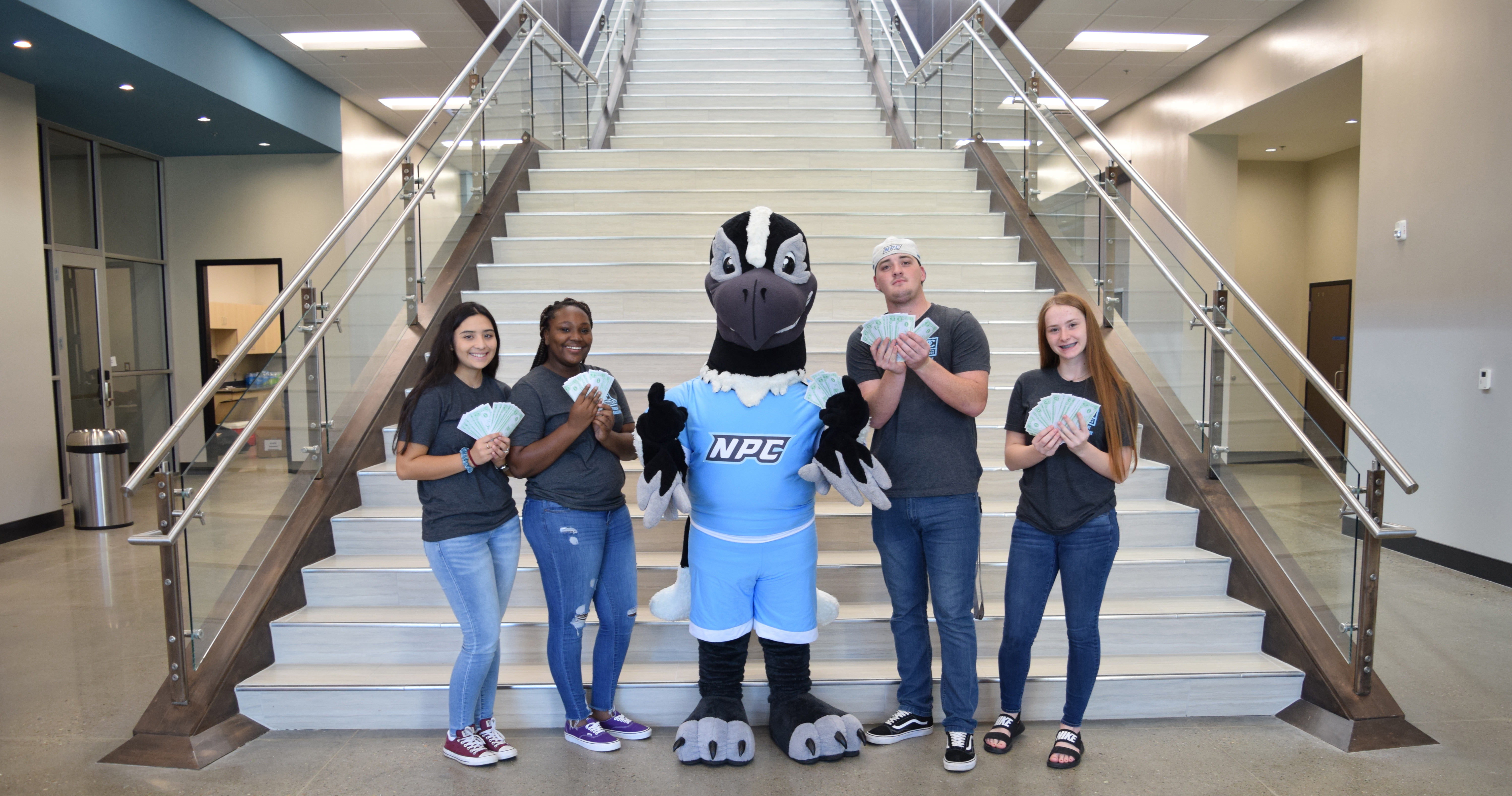 Students holding money with the mascot on the stairs