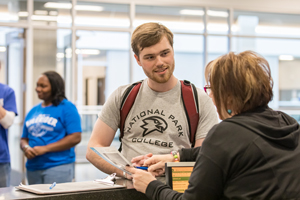 Person with a backpack in front of a desk with a person assisting them.