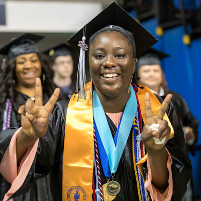 Tikima Simpkins in cap and gown at graduation holding up peace signs.