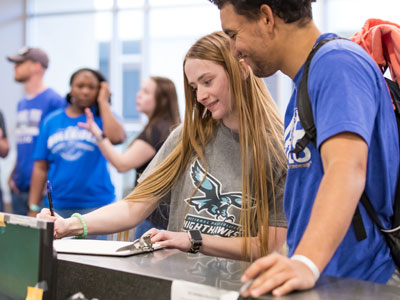 Two students standing at desk filling out a form