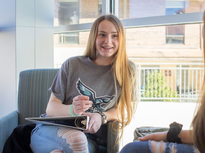 Girl sitting in chair in front of a window holding a 3-ring binder.