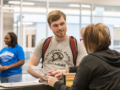 Student standing at desk talking to a person behind the desk.