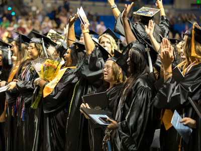 Graduates in cap and gowns with hands in the air