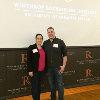 Stevie and Chris Wells standing in front of a projected Winthrop Rockefeller Institute sign for a photo.
