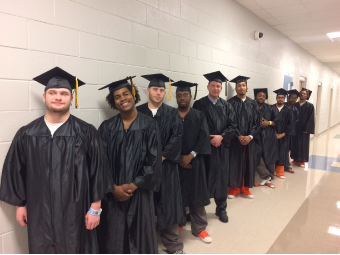 Ten graduates lined up in a single file line, in their cap and gowns for a photo.