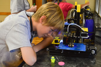 ITC bootcamp student leaning close to a 3D printer and reviewing to see how the machine works.