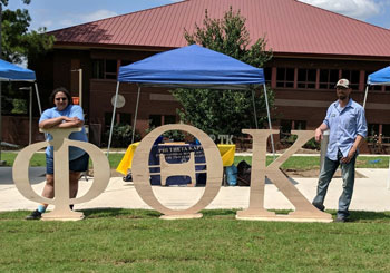 Members of PTK stand next to 4 foot wooden cutouts of the Phi Theta Kappa symbol.