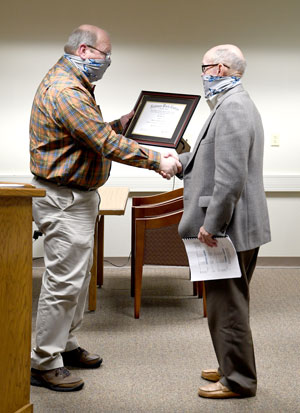 Trustee Jim Hale handing Trustee Don Harris a diploma and shaking his hand.