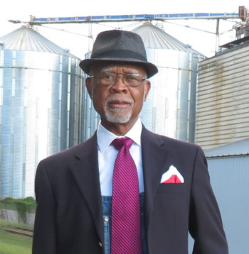Elmer Beard in a suit and tie standing in front of silos
