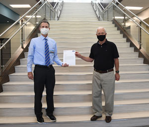 Dr. John Hogan and Larry Stanley holding a piece of paper while standing on stairs.