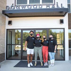 Four students in masks standing in front of doors to Dogwood Hall