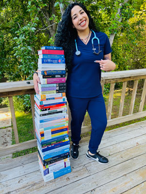 Sarah Duran standing on wood deck with her stack of nursing books.