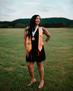 Sarah Duran standing in a field with a black dress on with her nursing and PTK stoles.