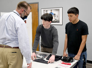 Two students showcasing their first aid wallet prototype to a male onlooker.