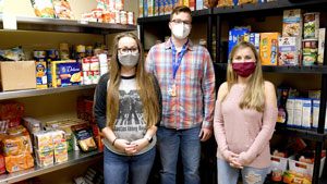 Three students standing in front of shelves of nonperishable food.