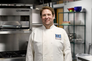 Jason Hunt in chef coat in front of stainless steel shelves.