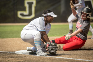 Softball player Kaylee Joseph on one knee on third base catching ball to tag runner out as she slides into third.