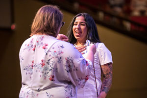 Student Sarah Duran in white scrubs receiving her pin from instructor.