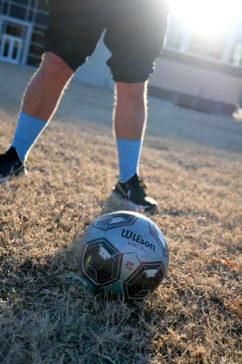 Male legs and feet standing on grass with a soccer ball in front of them. 