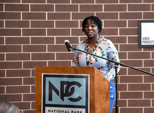 Tikima Simpkins standing behind podium reading her poem "Rise Up."