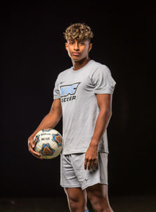 Adam Cerna standing against black backdrop in soccer jersey holding soccer ball.