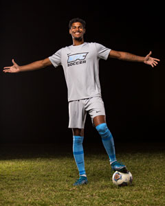 Soccer player Adrian Quintero standing on field with one foot on the ball and his arms stretched out to the side.