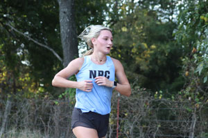 Cross Country runner Brooke Wyatt in tank top and shorts running in front of trees.