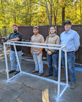 Four students standing behind soccer goal that they welded.