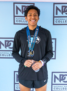 Miguel Mendez in cross country uniform standing in front of NPC backdrop holding medal