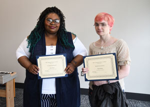 Two females standing in front of wall holding certificates.
