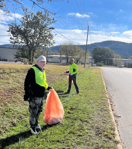 Two people in reflective vest picking up trash.