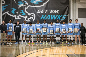 The sophomore men's basketball players standing on the court with pictures of themselves.