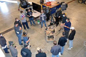 Students standing in circle around a wooden cart with tools and a laptop on it.