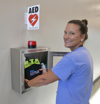 Campus Nurse Miki Smith placing an AED inside a metal box on the wall.