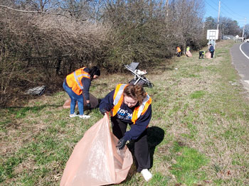 Several people in the grass beside a road picking up trash.