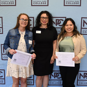 Three people standing in front of NPC blue background, two holding certificates.