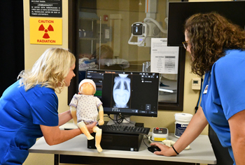 Two people standing in front of a monitor with an x-ray on it. One is holding a baby the other is pointing to the screen.