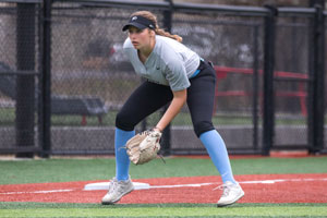 Katie Brach squatting with her glove close the ground ready to catch the ball.