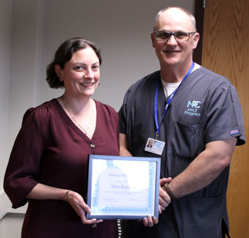 Two people standing next to each other, one in scrubs the other holding a certificate.