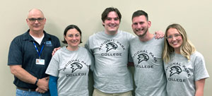 Five people standing in National Park College shirts against a wall.