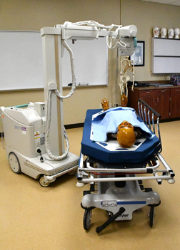 Portable xray machine taking a picture of a medical dummy on a stretcher.