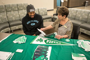 Evret Rice sitting at a table donned in University of Arkansas Monticello gear talking to a UAM rep.