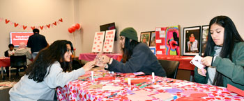 People sitting at a long table with different items to make Valentine's Day cards.